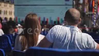 可爱的夫妇坐在市中心的蓝色椅子上，坐在会议上听讲座。 盖盖